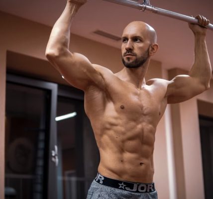 A bald, muscular man performing exercise on gym equipment indoors.